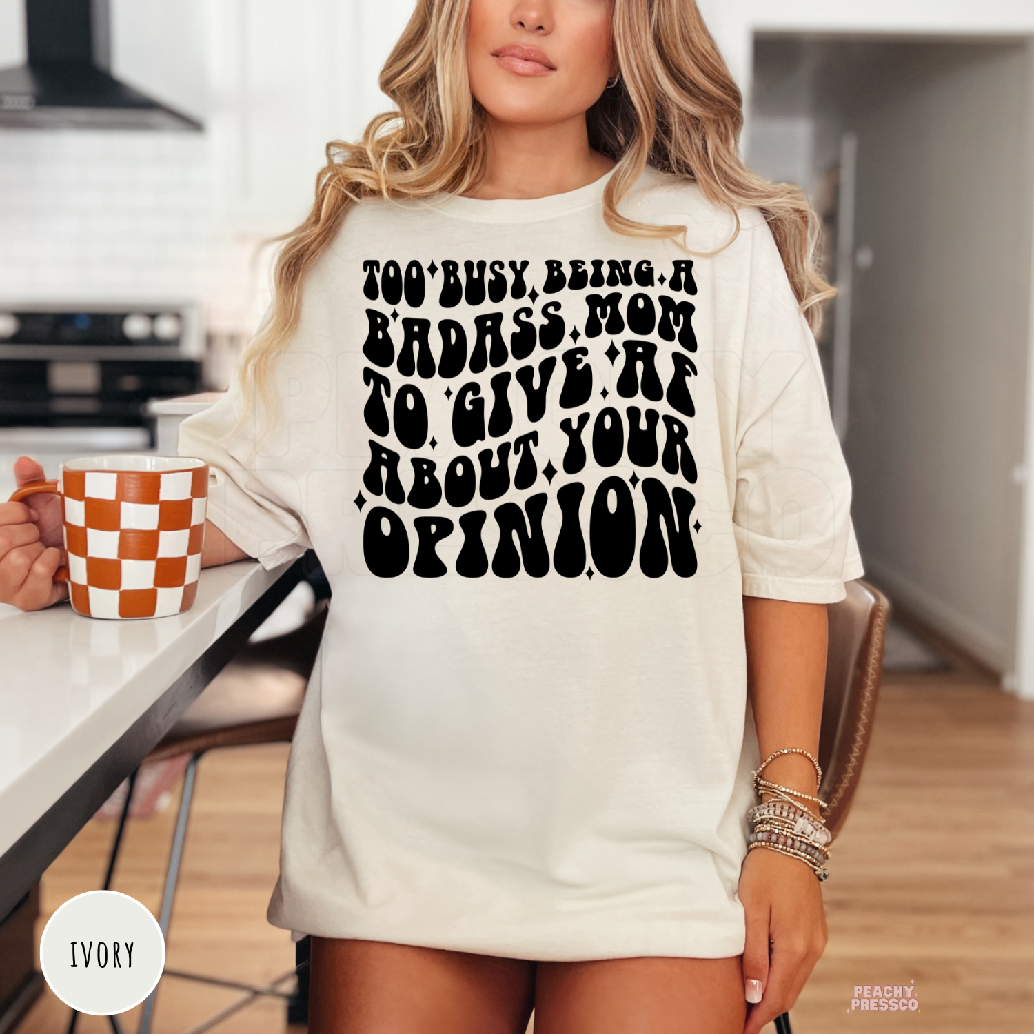 Ivory t-shirt featuring the bold "Too Busy Being a Badass Mom to Give AF About Your Opinion" graphic. Funny mom tee for everyday wear, Mother's Day, and busy moms.