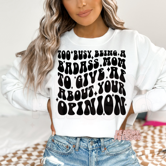 White sweatshirt featuring the bold "Too Busy Being a Badass Mom to Give AF About Your Opinion" graphic. A funny and stylish gift for moms who embrace confidence and humor.