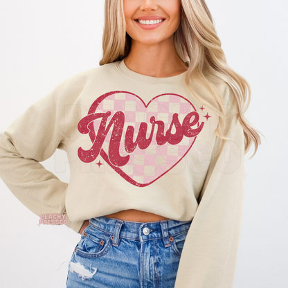 Sand crewneck sweatshirt displaying a vintage Nurse script over a soft pink checkered heart with a Valentine's Day aesthetic.
