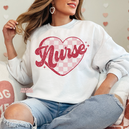 White crewneck sweatshirt showcasing a distressed Nurse script with a pink gingham heart for a trendy Valentine's nurse outfit.