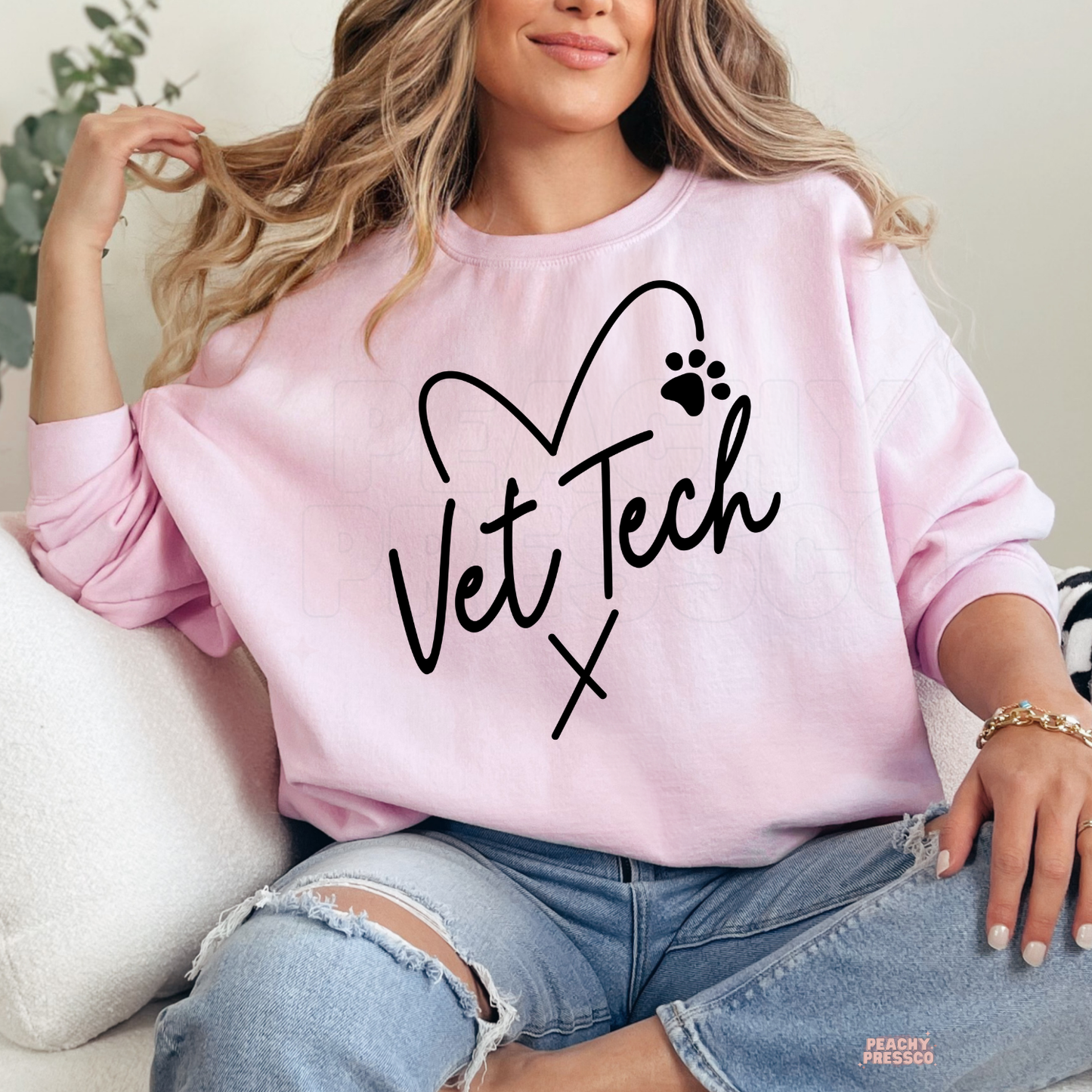 Woman wearing a light pink sweatshirt with a Vet Tech heart paw print design, a thoughtful gift for veterinary technicians and vet assistants.
