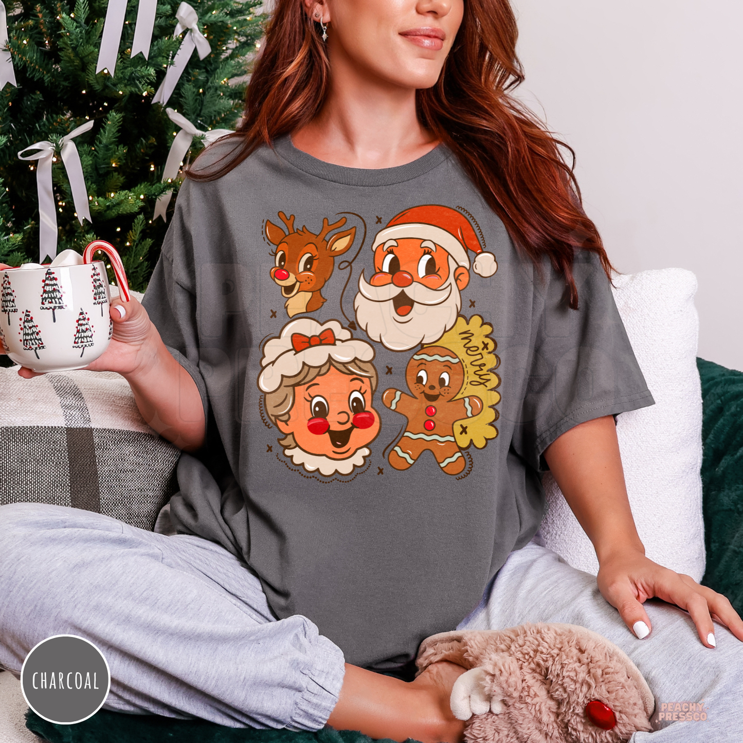 Woman holding a holiday mug wearing a charcoal grey t-shirt featuring retro Santa Claus, Mrs. Claus, Rudolph, and gingerbread.