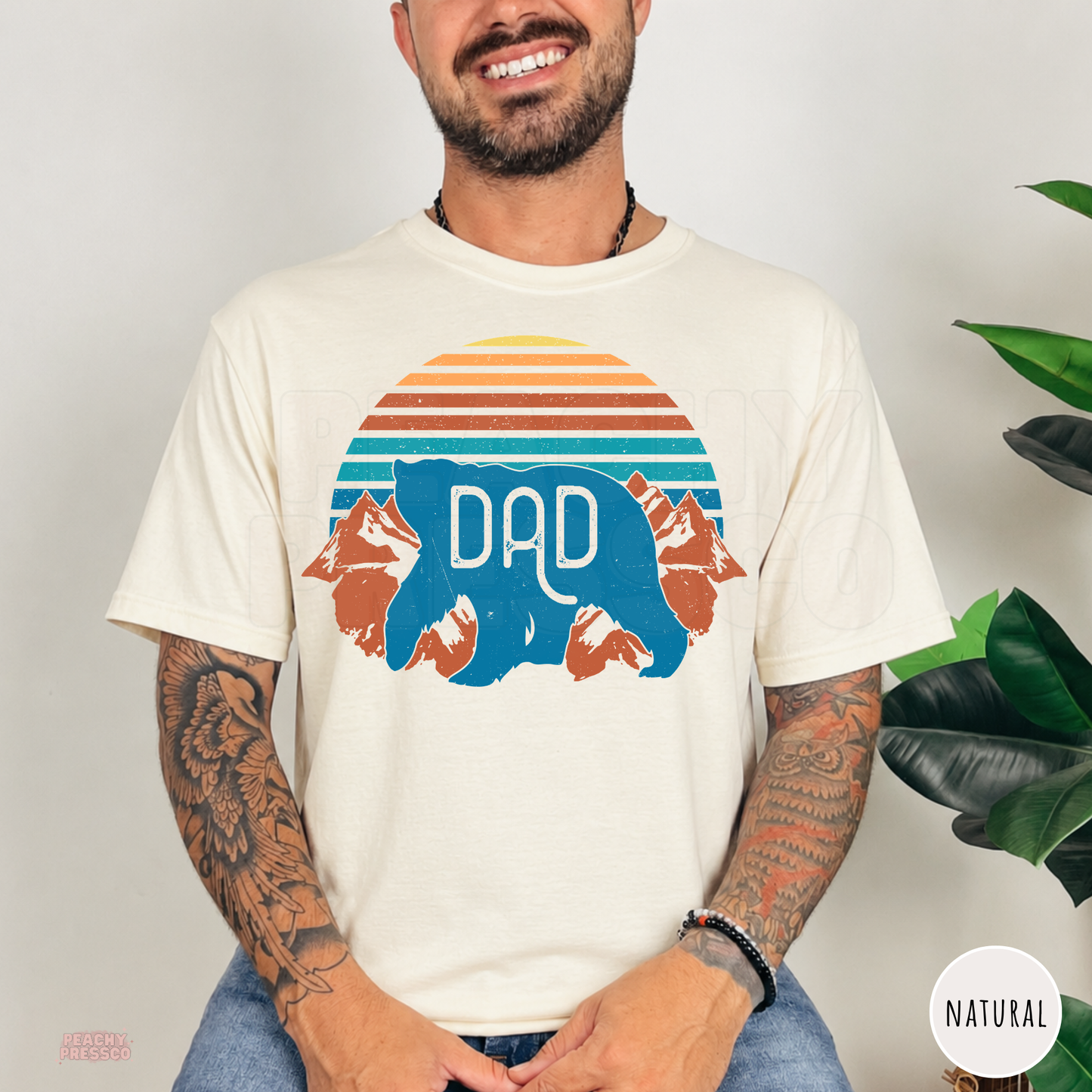 Natural t-shirt featuring a retro sunset, mountain peaks, and blue Dad bear graphic, perfect for camping and outdoor dads.