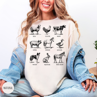 Woman wearing a natural sweatshirt featuring vintage farm animals with their sounds including baa, cluck, moo, oink, neigh, quack, woof, squeak, and hee-haw.
