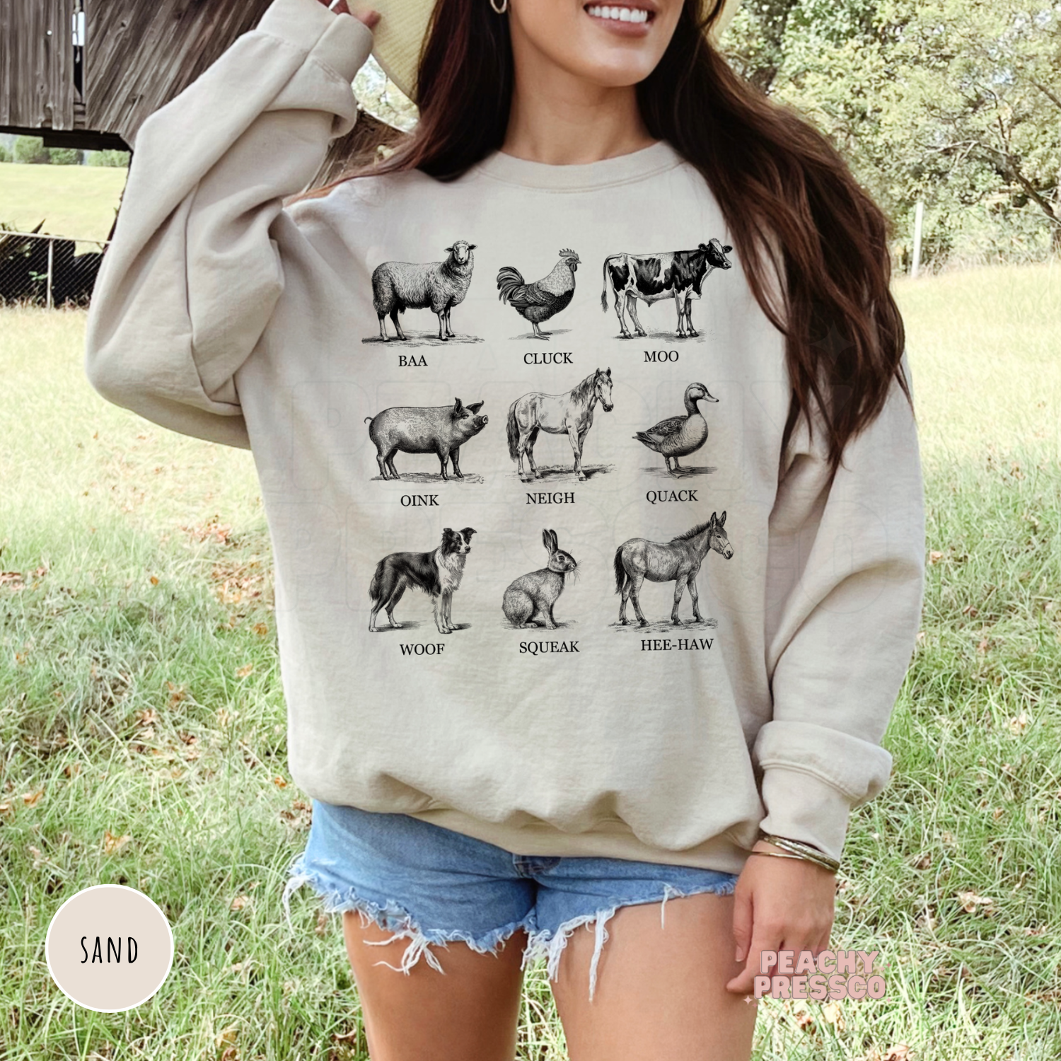 Woman wearing a sand sweatshirt with a vintage farm animal sounds graphic featuring sheep, rooster, cow, pig, horse, duck, dog, rabbit, and donkey.