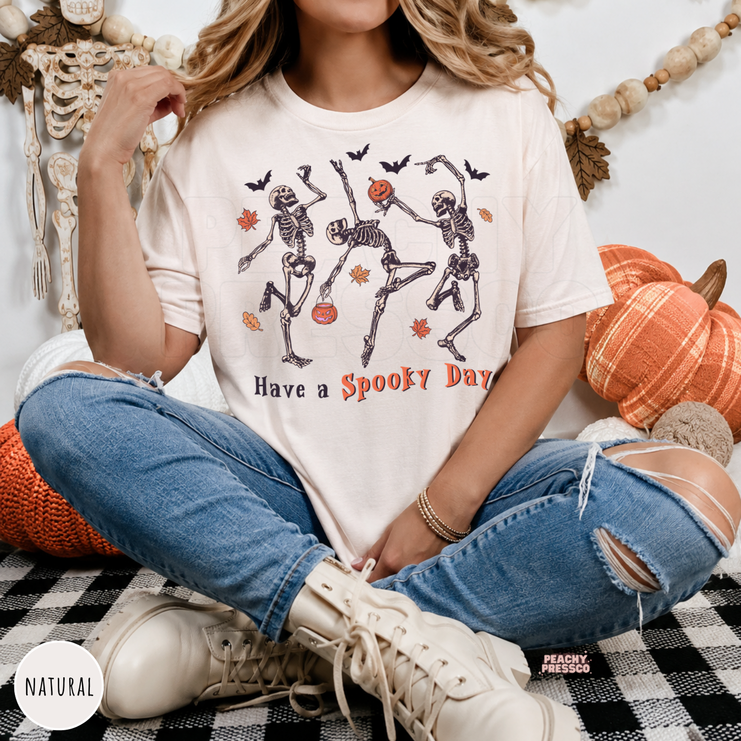 Woman wearing a natural Halloween graphic tee with dancing skeletons, pumpkins, bats and "Have a Spooky Day" design.