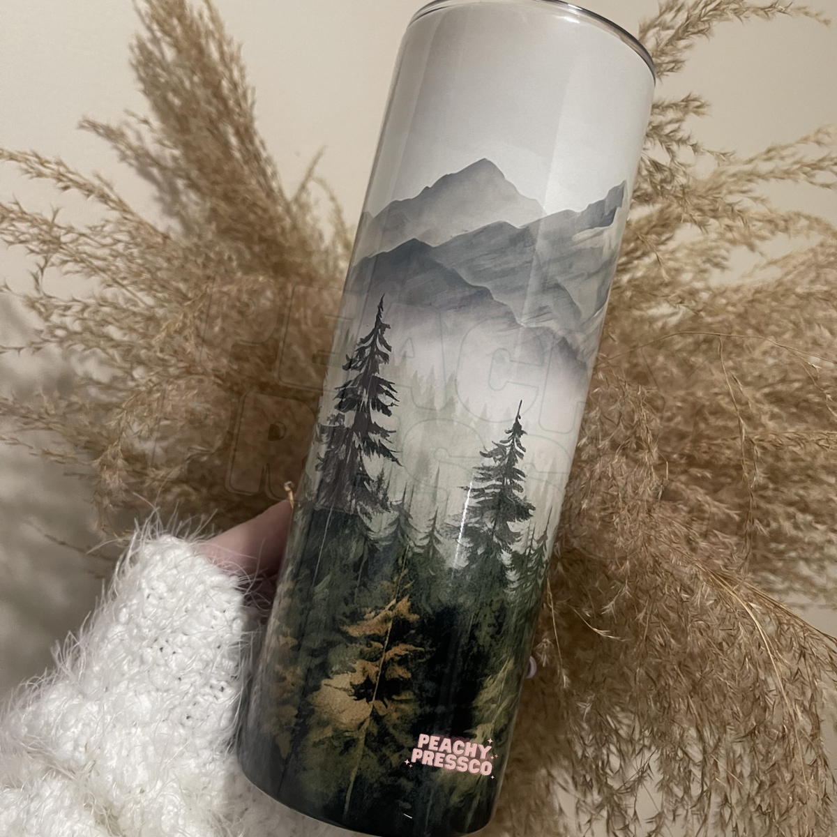 20oz skinny tumbler featuring a watercolor mountain landscape with evergreen forest and misty wilderness design.