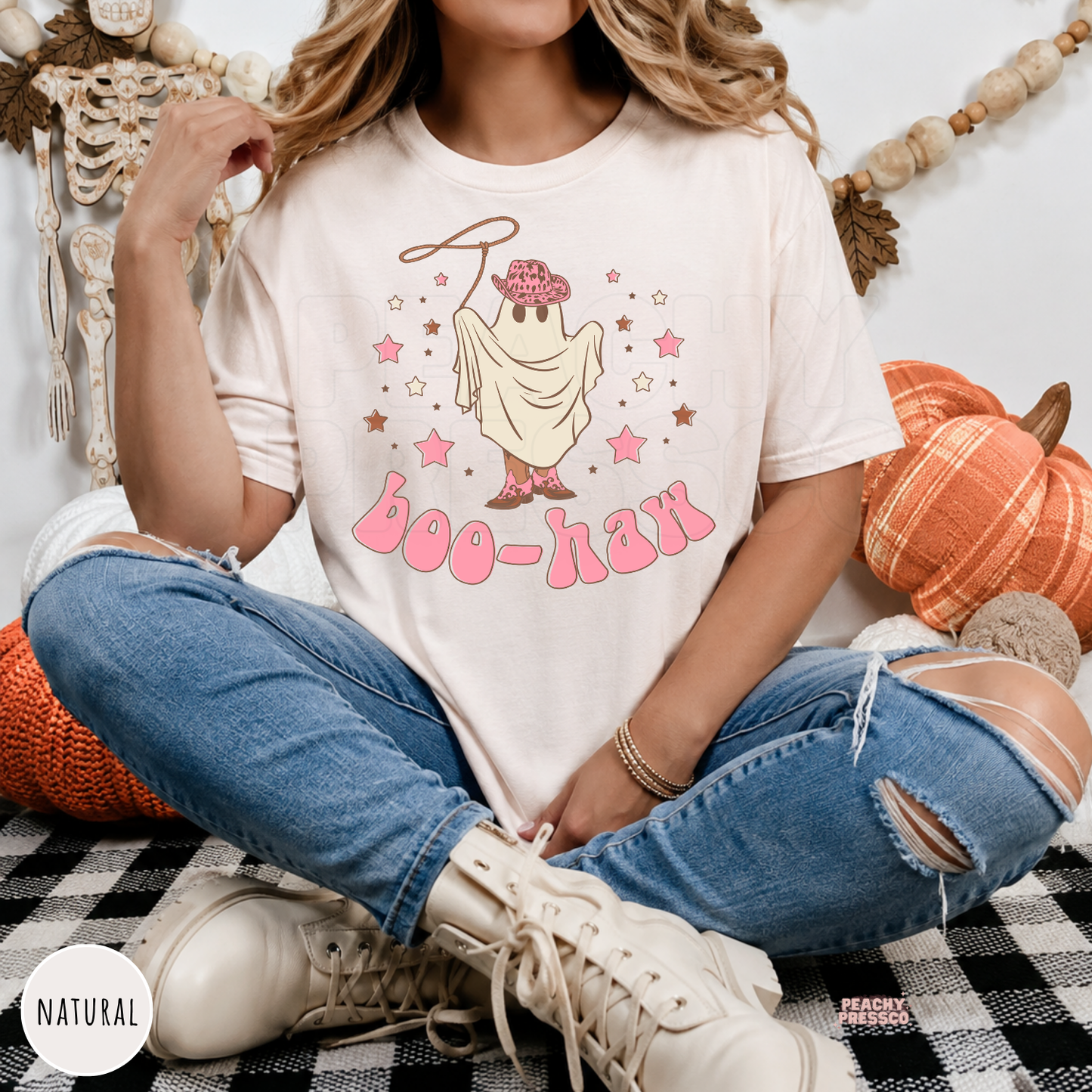 Woman wearing a natural colored Halloween t-shirt featuring a cowgirl ghost with pink cowboy hat, boots and Boo-Haw lettering.