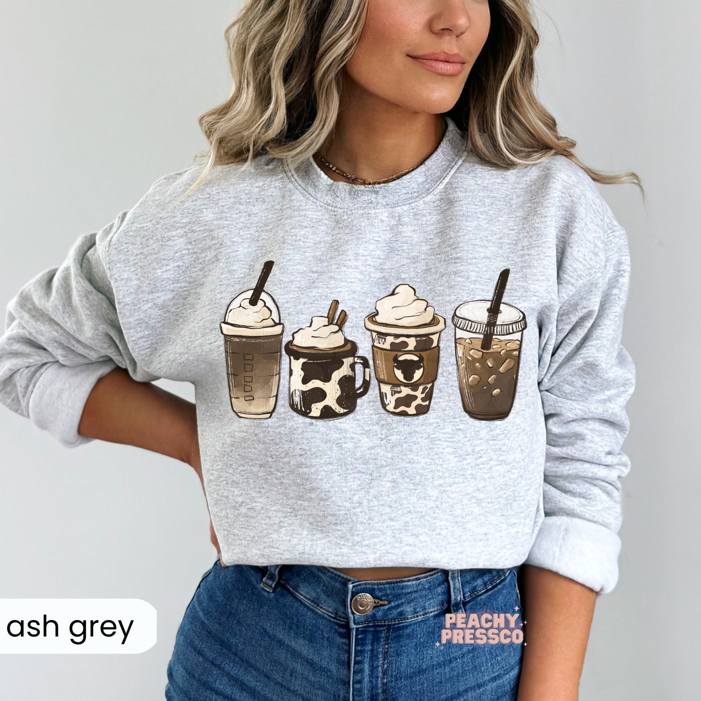 Woman wearing an ash grey sweatshirt with a western coffee drinks graphic featuring iced coffee, hot coffee, latte, and frappé illustrations.
