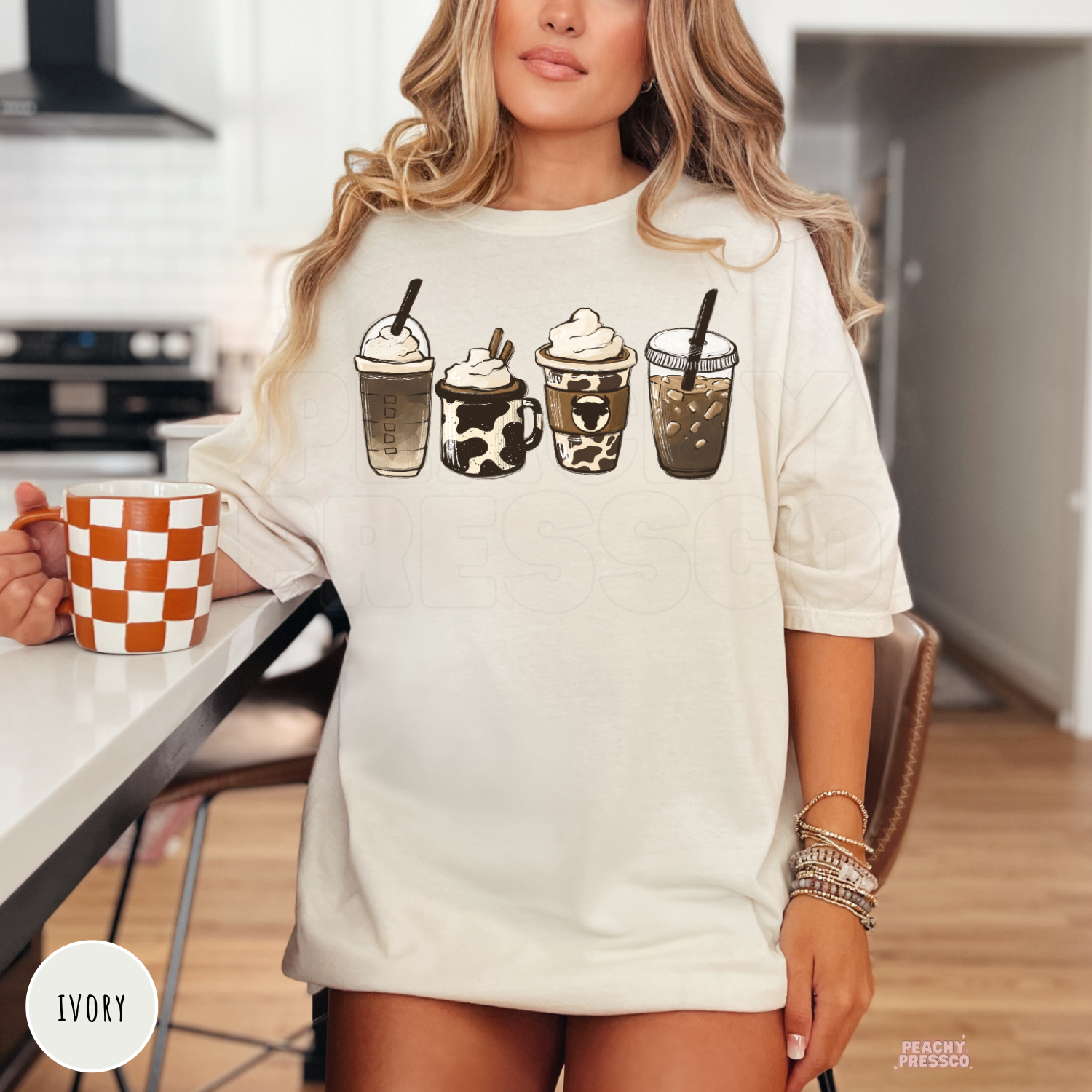 Woman wearing an ivory t-shirt featuring a western coffee lover design with four rustic coffee drink illustrations in neutral brown tones.