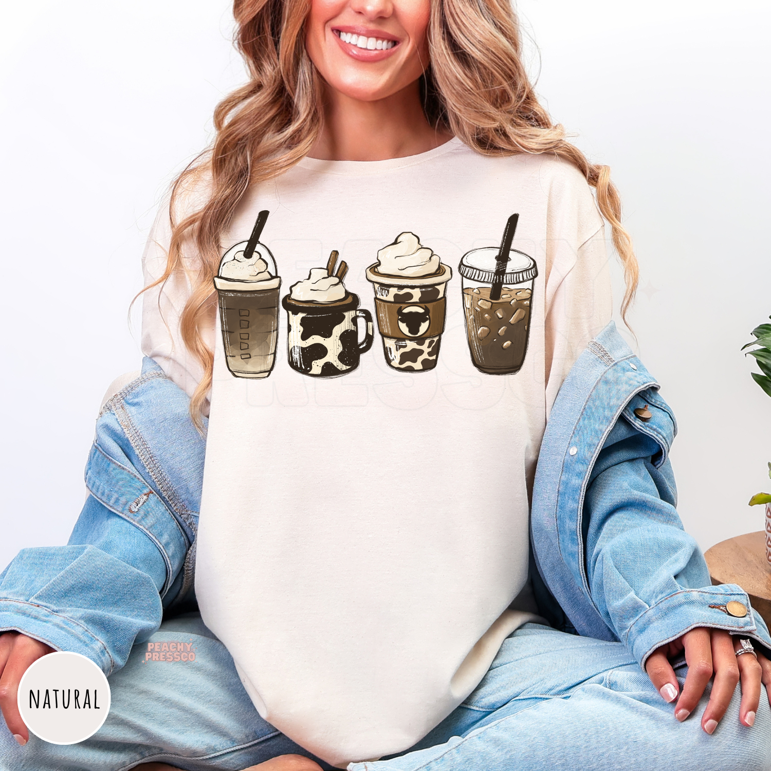 Woman wearing a natural shirt featuring four western-inspired coffee drinks with cow print accents, including iced coffee, latte, and frappé illustrations.