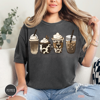 Woman wearing a pepper Comfort Colors t-shirt featuring a western coffee drinks graphic with cow print coffee cups and rustic café aesthetic.