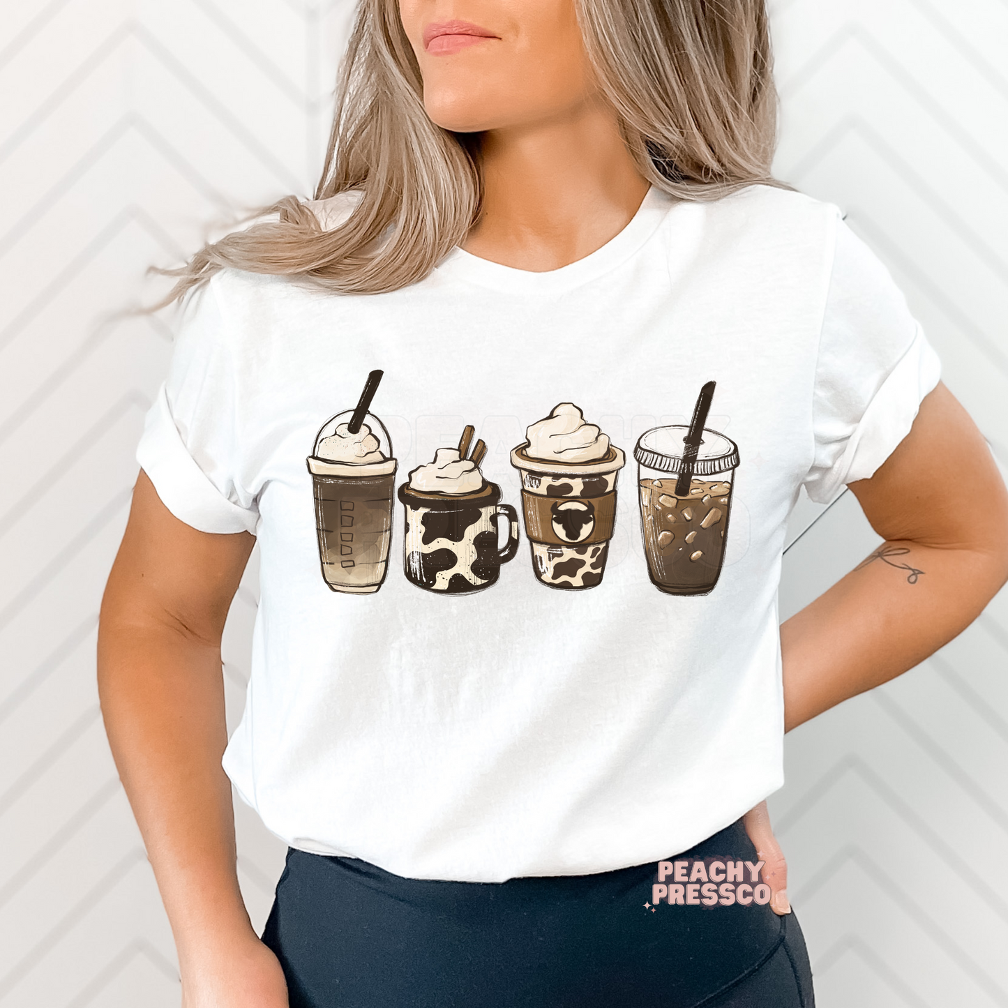 Woman wearing a white t-shirt featuring four western-inspired coffee drinks with neutral tones and cow print coffee cup illustrations.