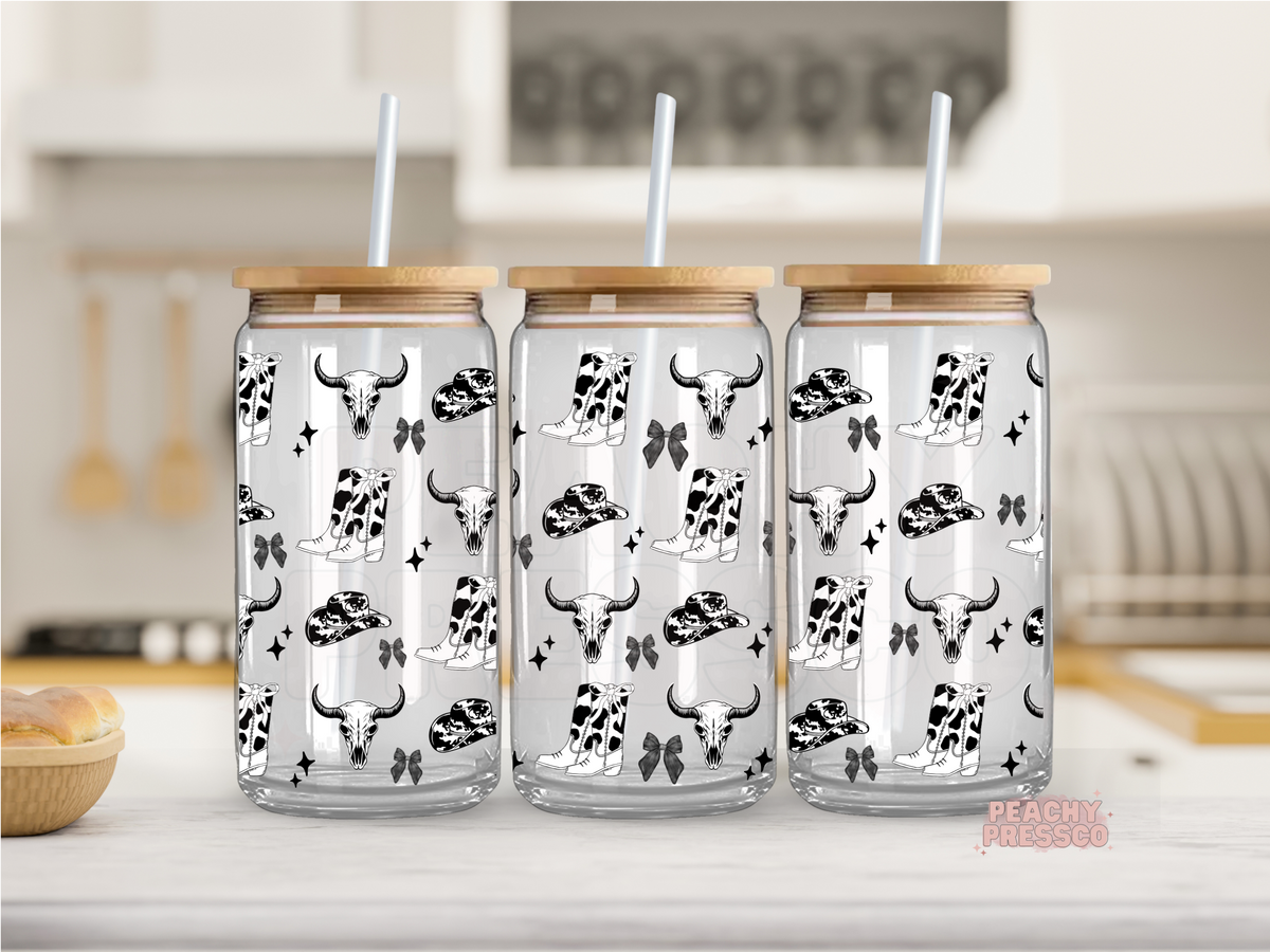 Glass cup with bamboo lids and white straws, decorated with a black and white cow skull and hat pattern, displayed on a kitchen counter.