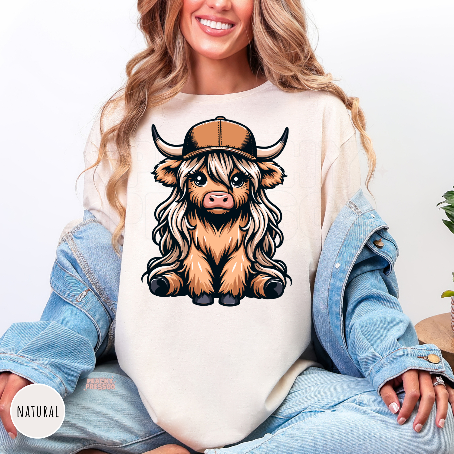 Natural colored shirt featuring a cute Highland cow with long hair and a trucker hat in western style.