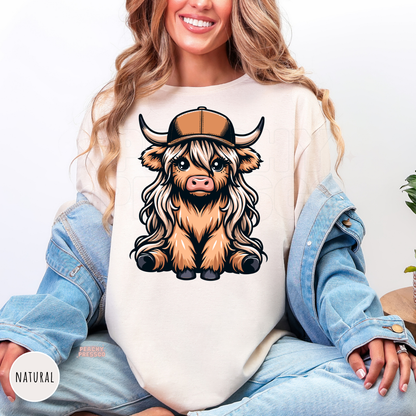 Natural colored shirt featuring a cute Highland cow with long hair and a trucker hat in western style.