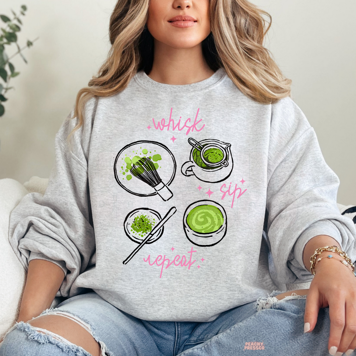 Ash grey Whisk Sip Repeat matcha sweatshirt featuring green matcha tea illustrations, bamboo whisk, matcha bowls, pink handwritten lettering, and sparkles.