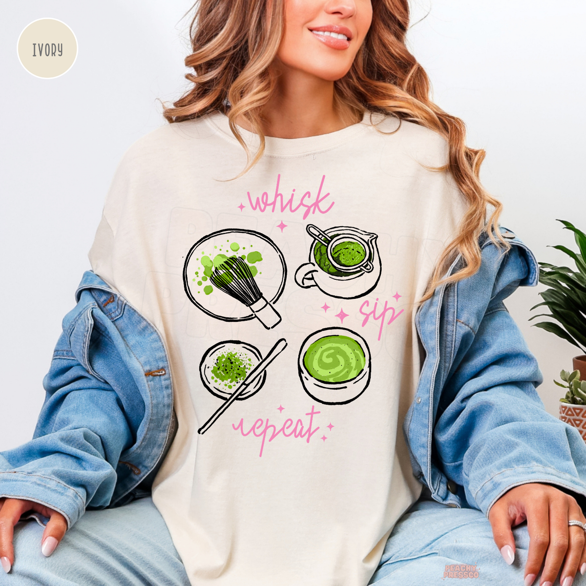 Ivory Whisk Sip Repeat matcha shirt featuring green matcha bowls, bamboo whisk, matcha powder, and pink script lettering with sparkling accents.