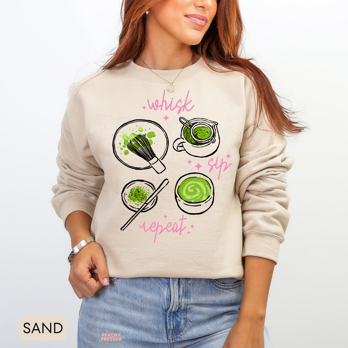 Sand Whisk Sip Repeat matcha sweatshirt with cute matcha tea bowls, whisk and powder illustrations, pink handwritten words, and playful sparkles.