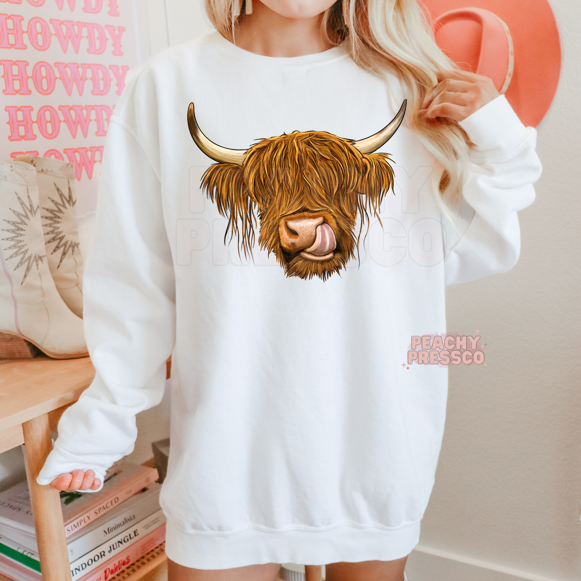 Woman wearing a white sweatshirt with a realistic Highland cow graphic, perfect for country western fashion and cozy farmhouse style.