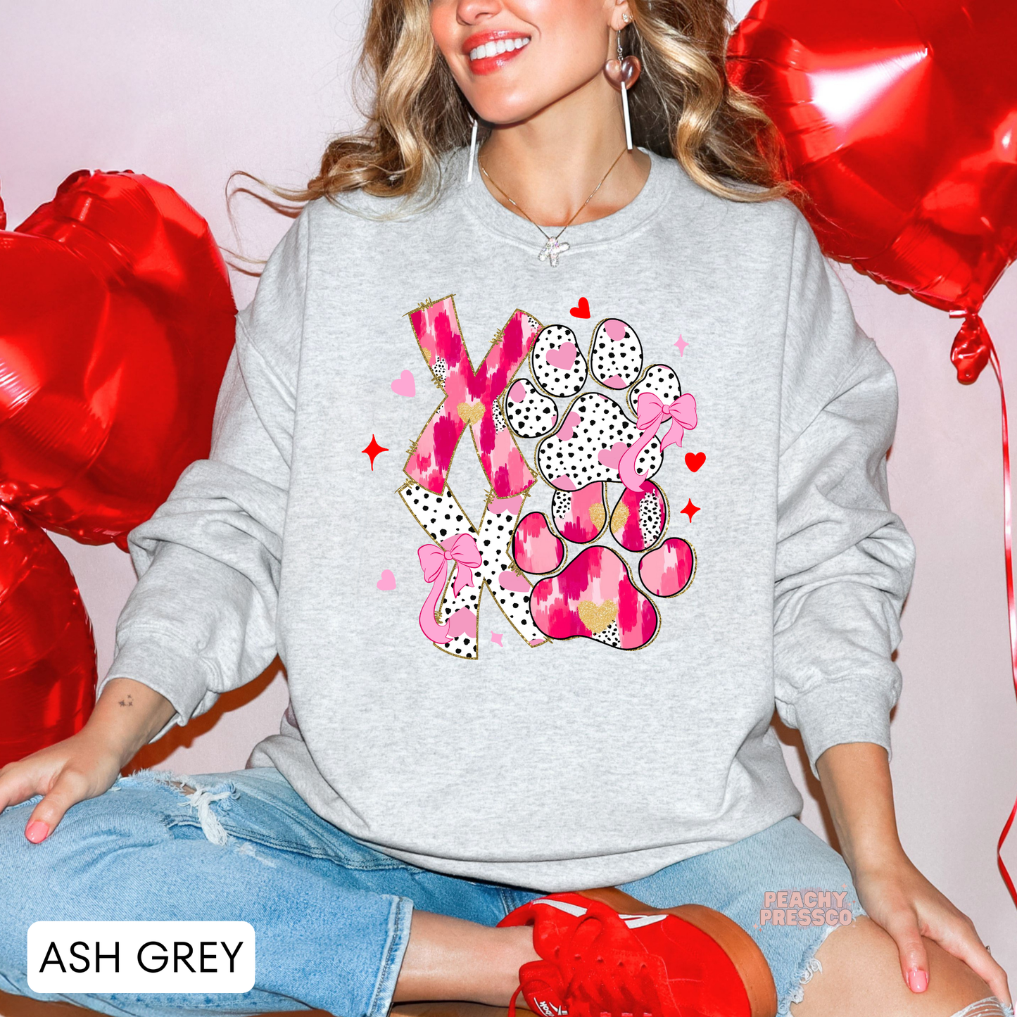 Ash grey sweatshirt displaying a colorful XOXO dog paw Valentine's design with pink accents, hearts, and decorative bows.