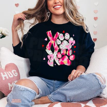Black crewneck sweatshirt featuring a vibrant pink XOXO dog paw graphic with playful hearts and bows for dog moms.