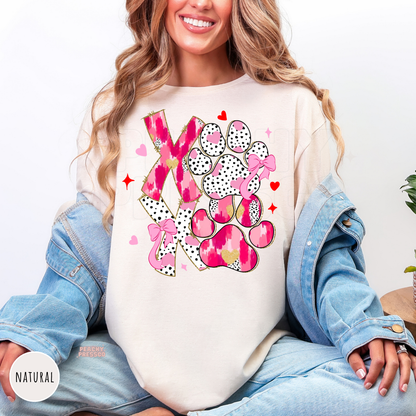 Natural shirt featuring a pink XOXO dog paw graphic with bows, hearts, and leopard-inspired details for Valentine's Day dog lovers.