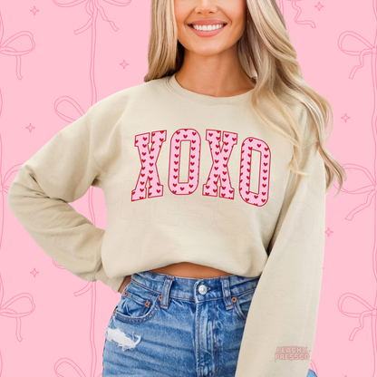 Cute XOXO varsity heart design printed on a sand crewneck sweatshirt with a minimalist Valentine's Day style.