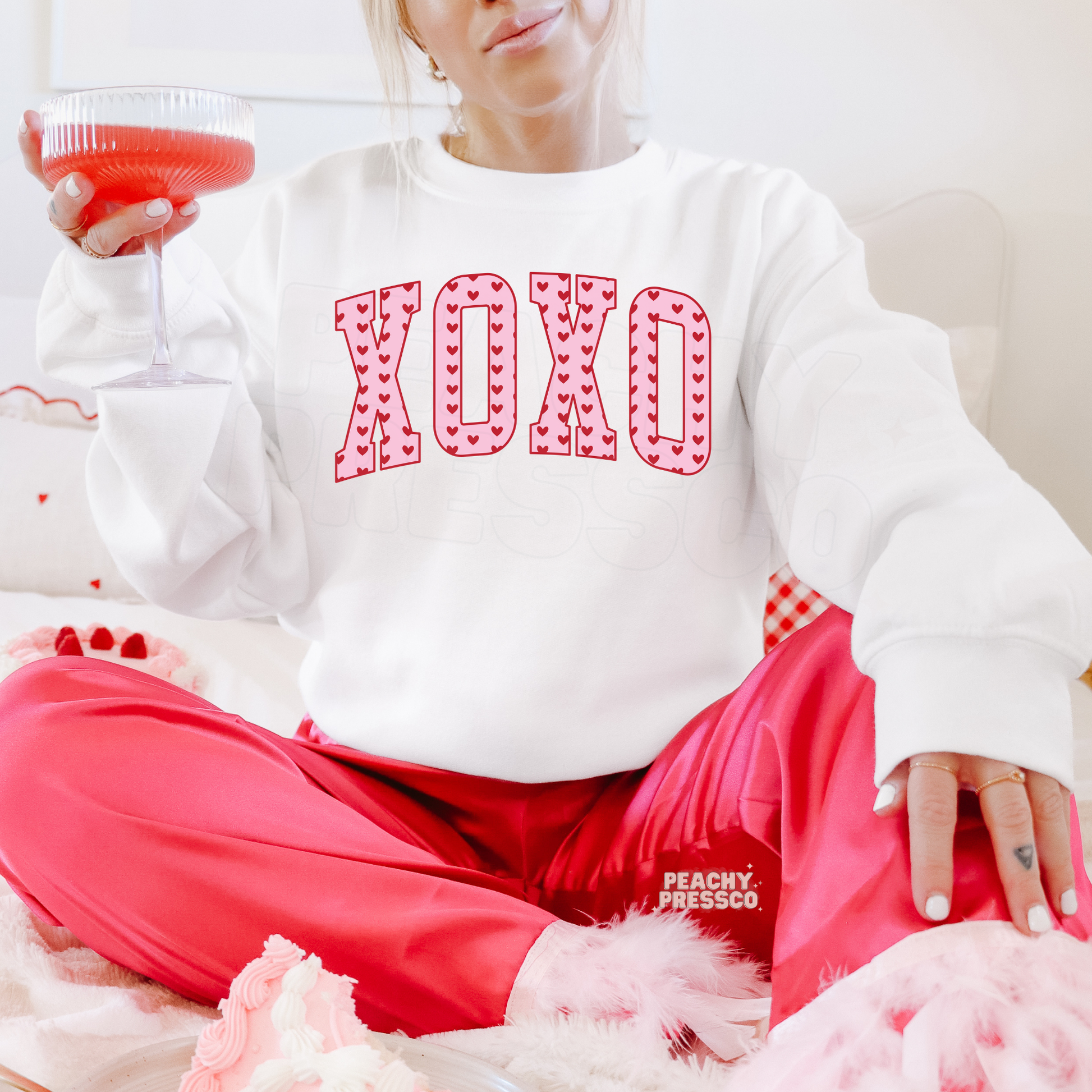 White crewneck sweatshirt featuring a retro XOXO heart graphic with varsity lettering and playful Valentine's Day design.