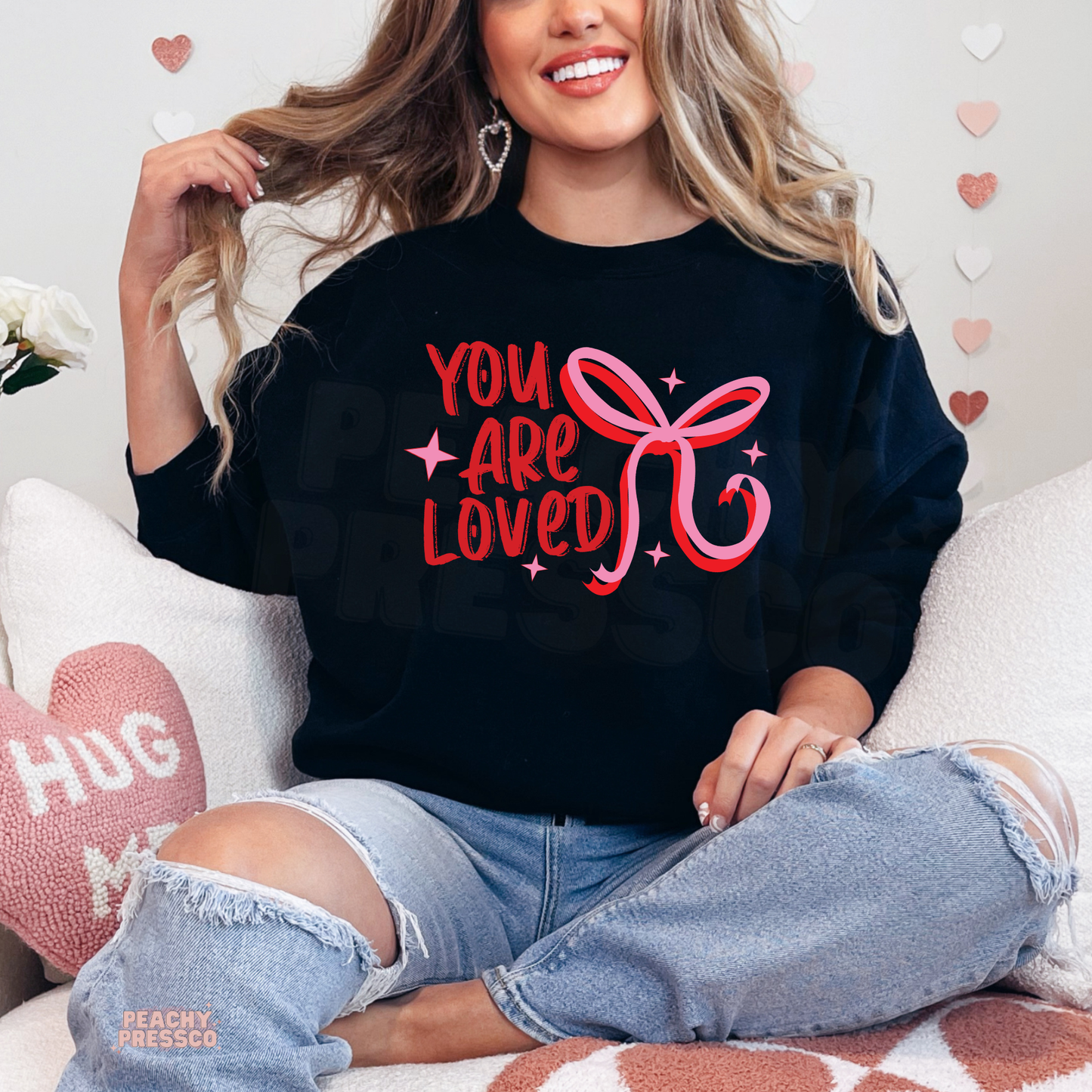 Black crewneck sweatshirt showcasing a bold red and pink "You Are Loved" design with a trendy coquette bow.