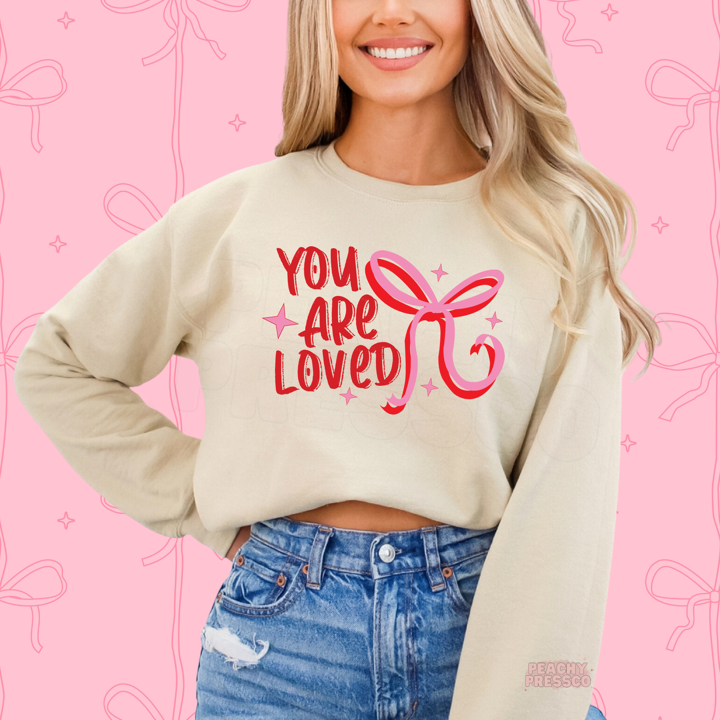 Sand crewneck sweatshirt featuring a vintage-inspired "You Are Loved" design with a pink bow for Valentine's Day gifting.