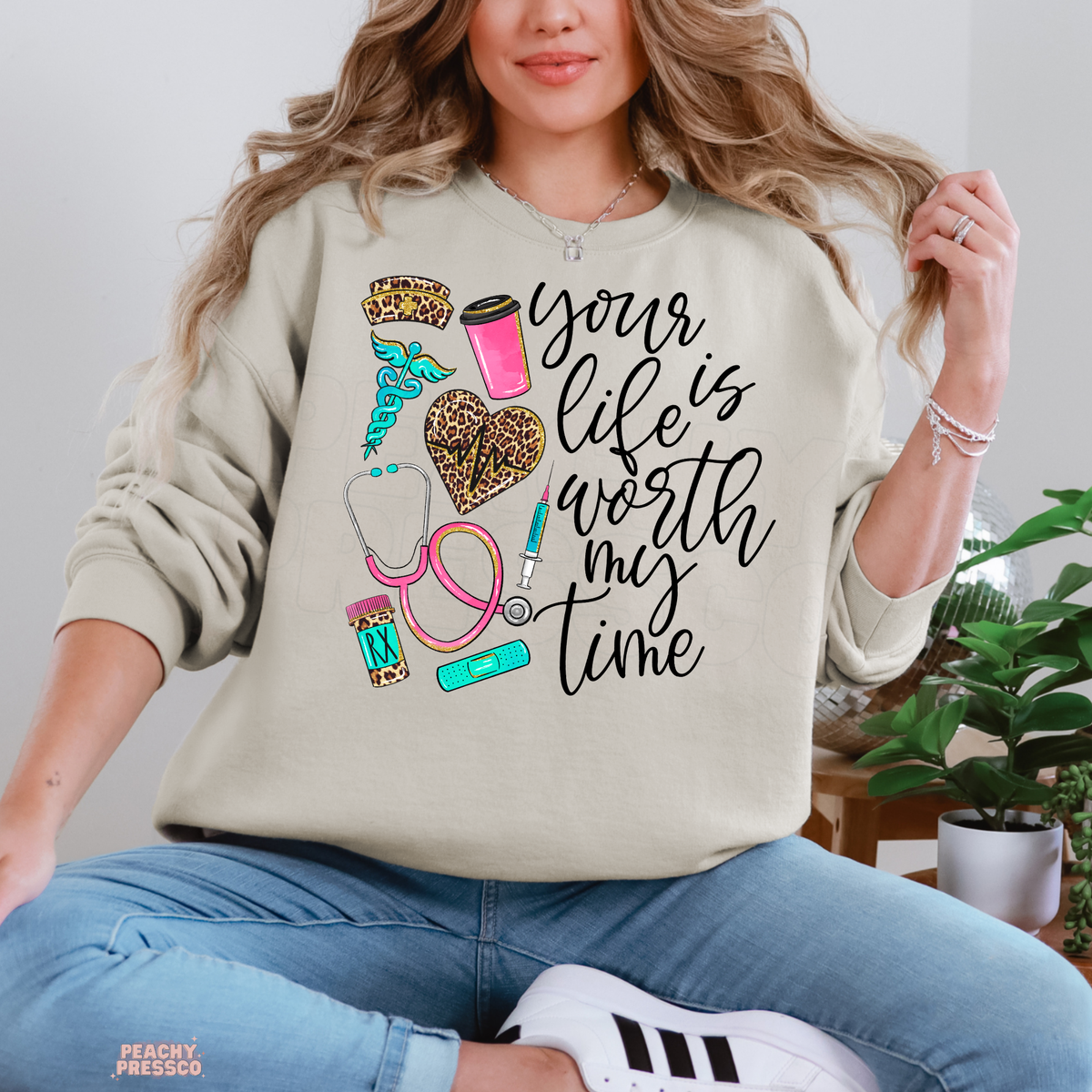 Sand nurse sweatshirt with Your Life Is Worth My Time quote, leopard print heart, pink stethoscope, nurse hat, coffee cup and medical graphics.
