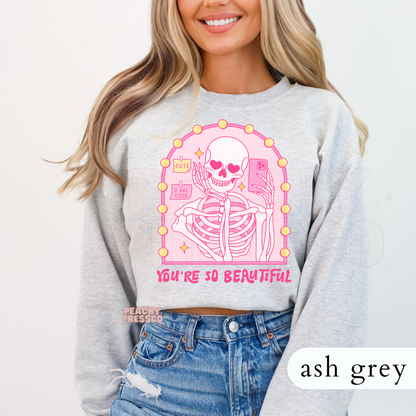 Ash grey sweatshirt featuring a pink coquette skeleton selfie illustration with heart eyes, vanity mirror, and "You're So Beautiful" graphic.