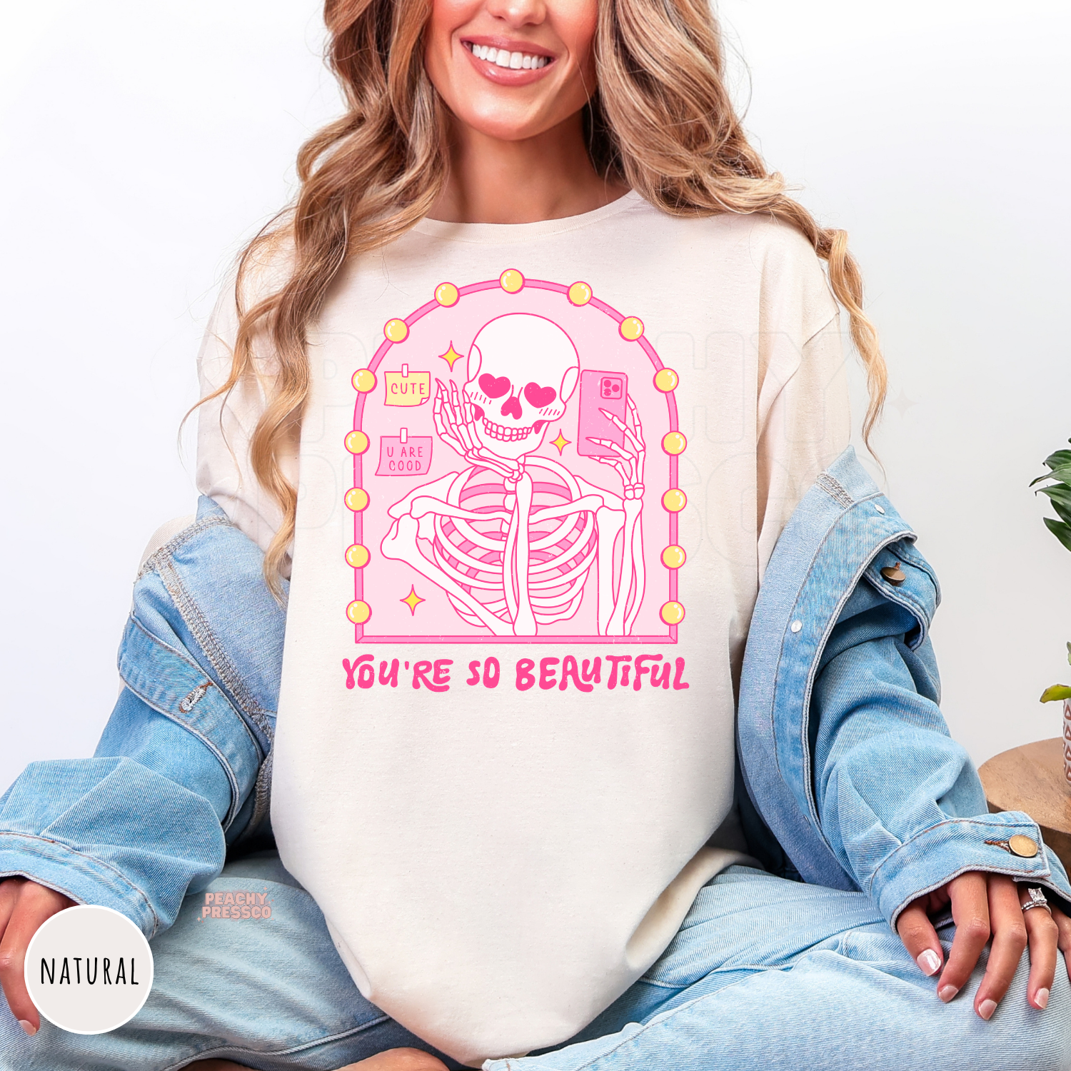 Natural t-shirt with a pink skeleton mirror selfie graphic featuring heart eyes, vanity mirror lights, and the quote "You're So Beautiful."