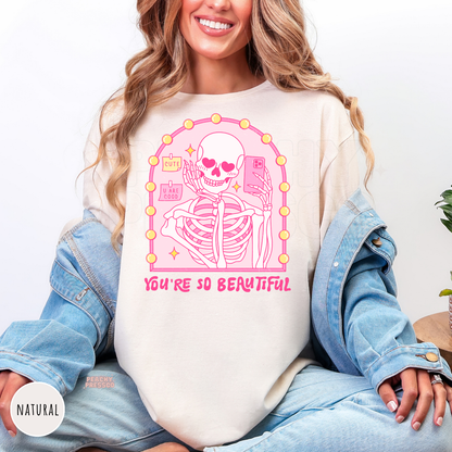 Natural t-shirt with a pink skeleton mirror selfie graphic featuring heart eyes, vanity mirror lights, and the quote "You're So Beautiful."